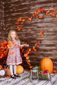 Little girl holds garaland of orange leaves in room with pumpkin